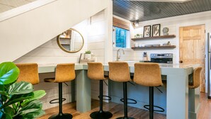 A modern kitchen with a bar area, wooden flooring, and a view of the outdoors. - The Treehouse-10mi from Oxford-Velvet Ditch Villas (Batesville)