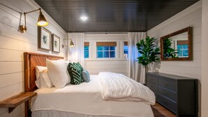 A bedroom with a wooden headboard, a large bed with white bedding, a dresser, and a mirror. - The Treehouse-10mi from Oxford-Velvet Ditch Villas (Batesville)