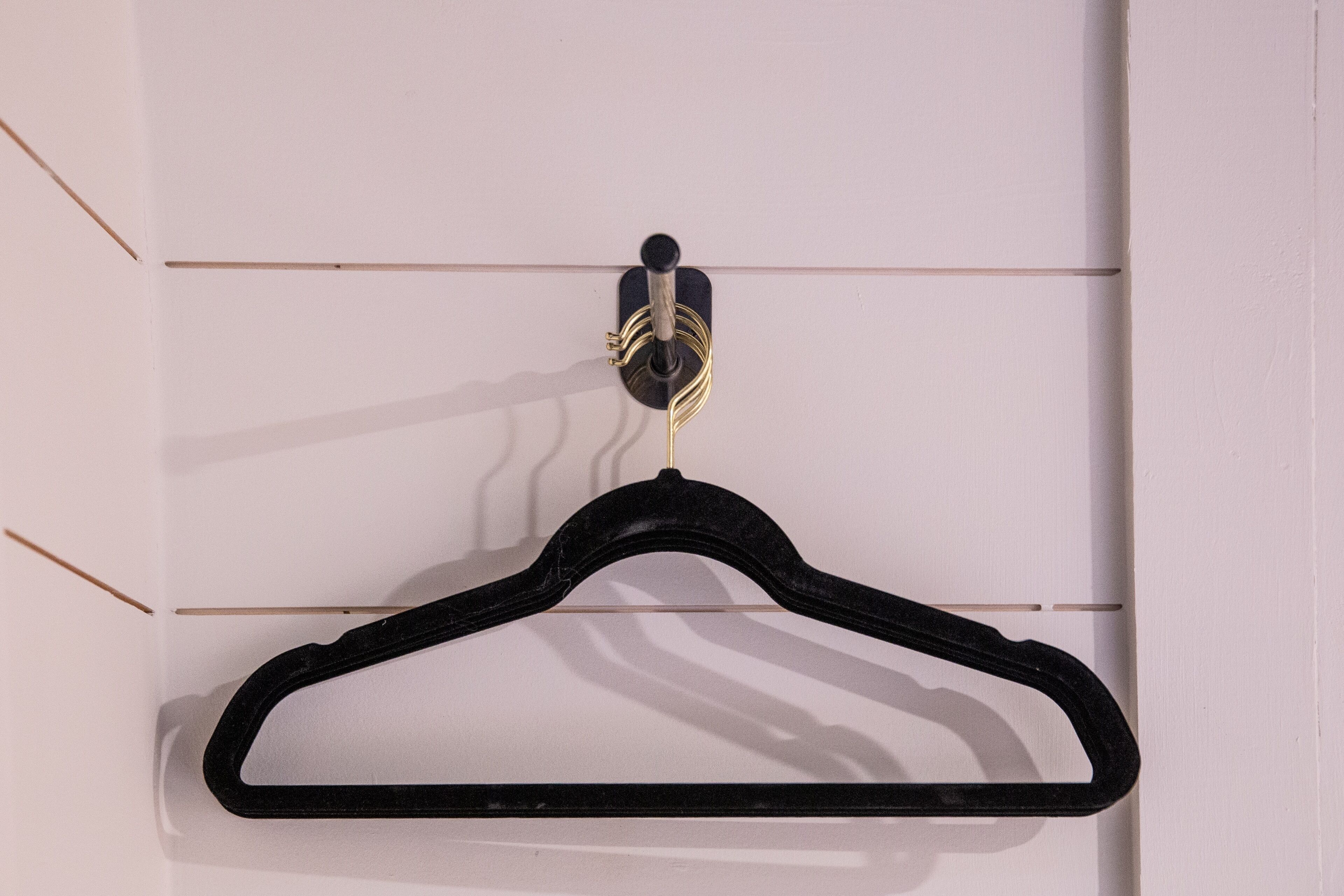 Un cintre noir avec un crochet de couleur or, fixé sur un mur blanc orné de lignes horizontales.