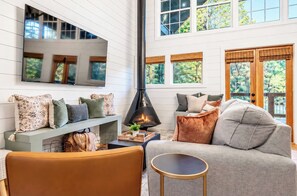 A modern living room with a fireplace, comfortable seating, and large windows.