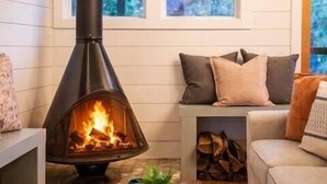Una sala de estar acogedora con una chimenea de leña, un sofá, una mesa de centro y un ventanal con vistas a árboles.