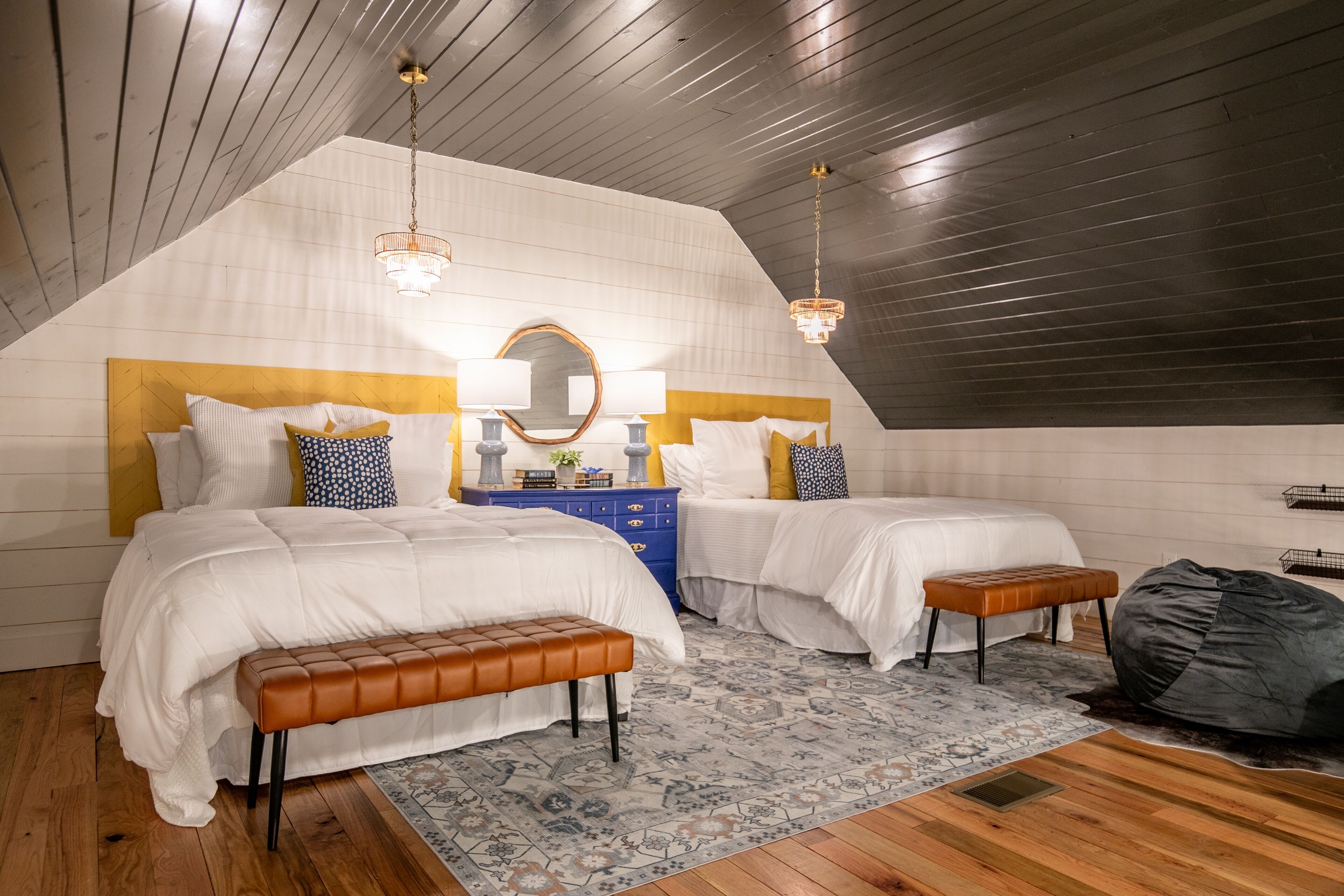 A bedroom with two beds, a bench, a dresser, and a mirror.