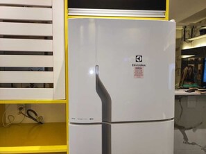 A white Electrolux refrigerator in a kitchen with yellow cabinets and a marble countertop.