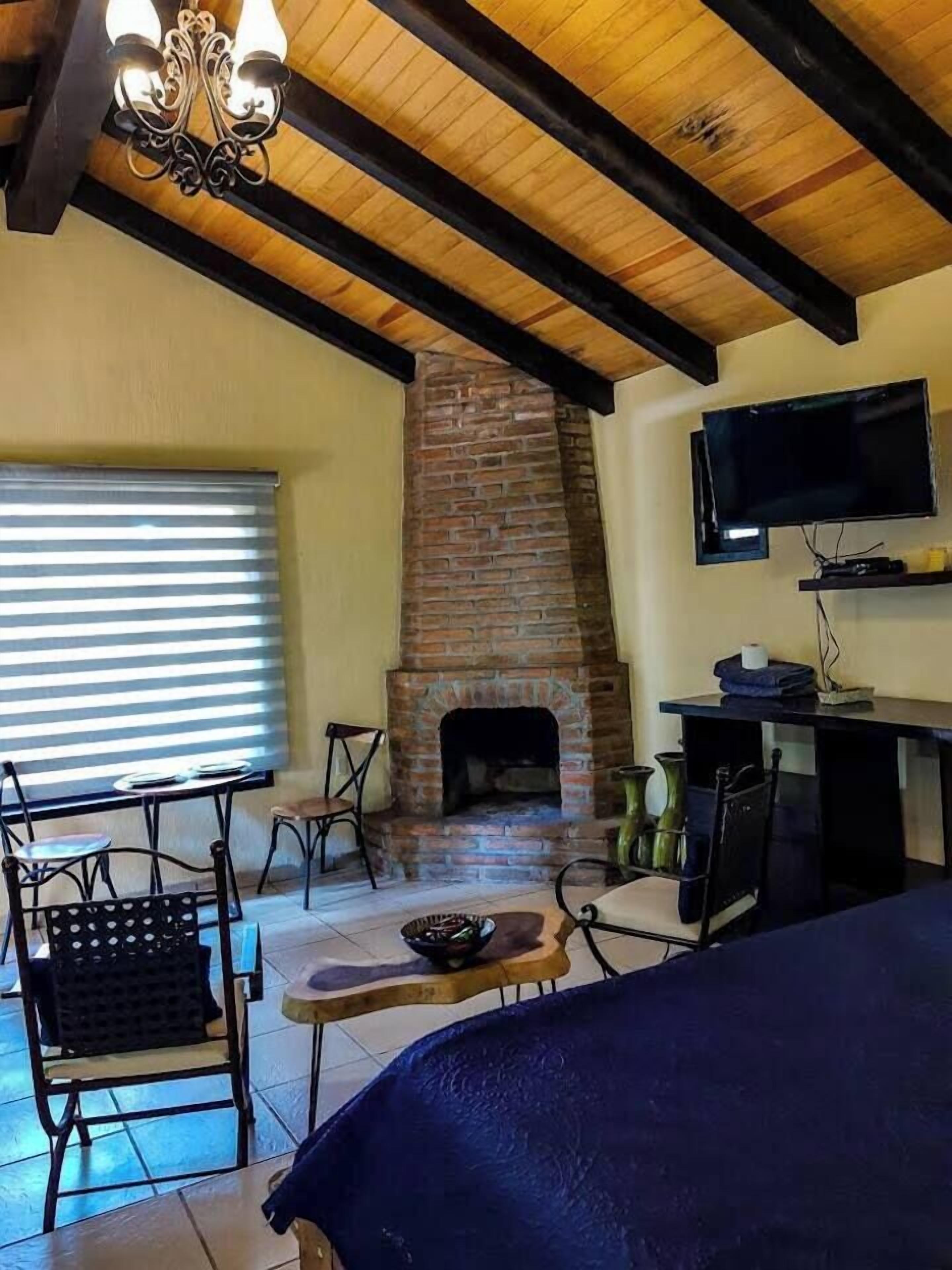 A cozy living room with a brick fireplace, a television, and a dining area with chairs and a table.