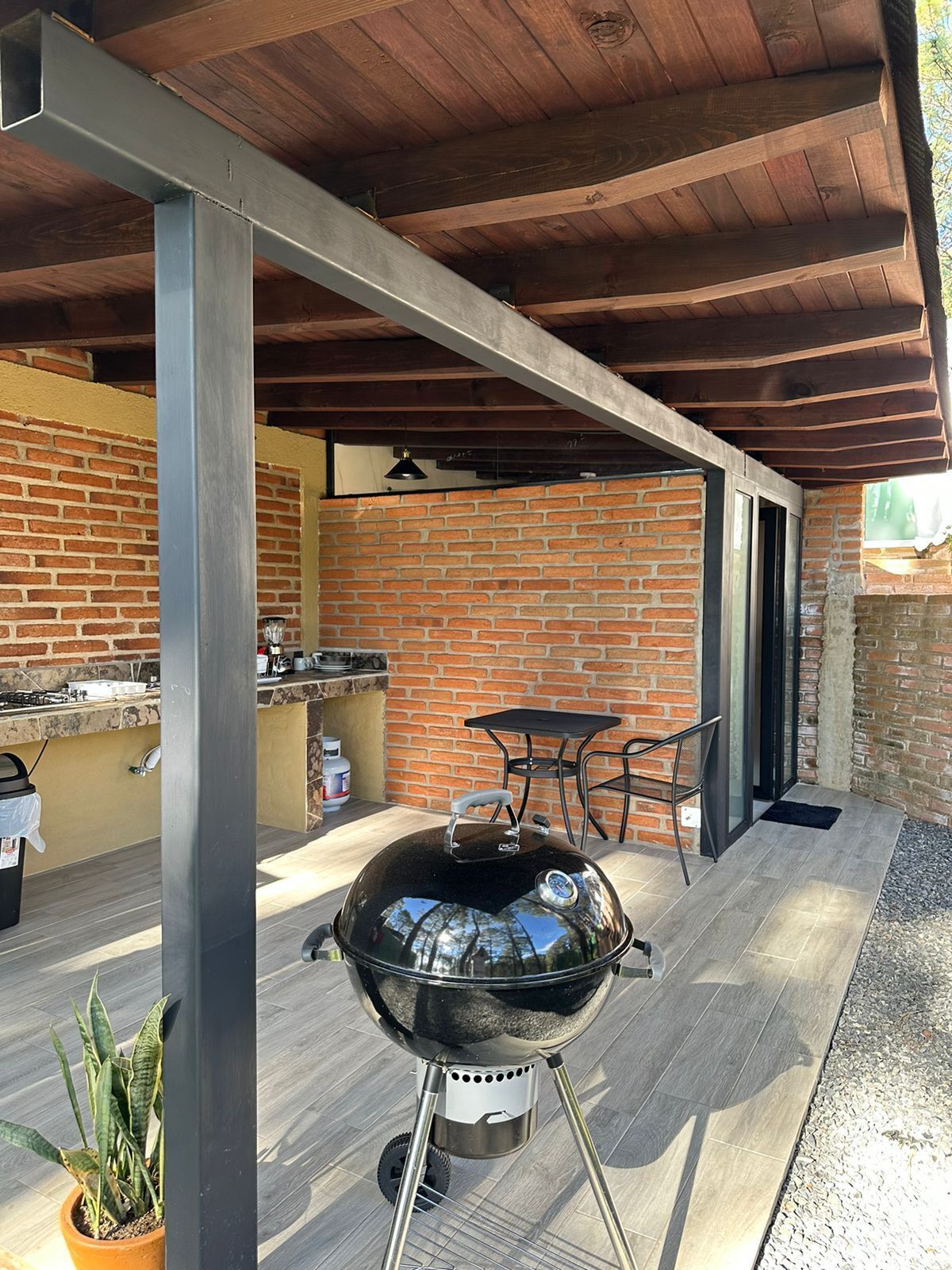 Un patio techado al aire libre con pared de ladrillo, una parrilla y una mesa con sillas.