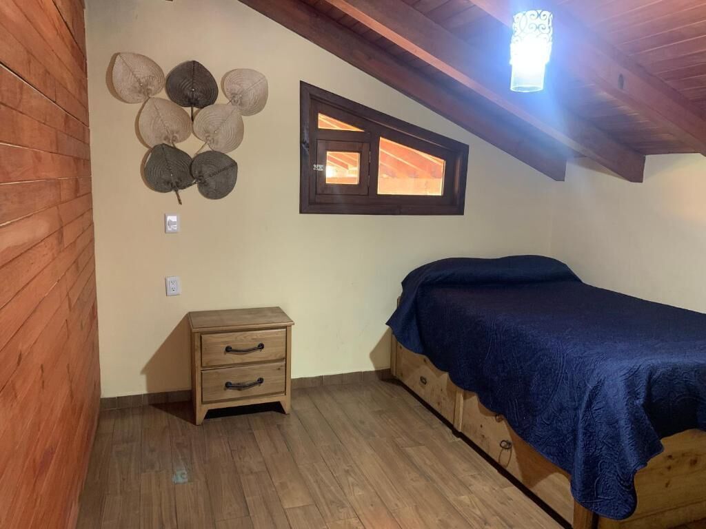 A bedroom with a wooden bed, a nightstand, a wall-mounted light, and a window.