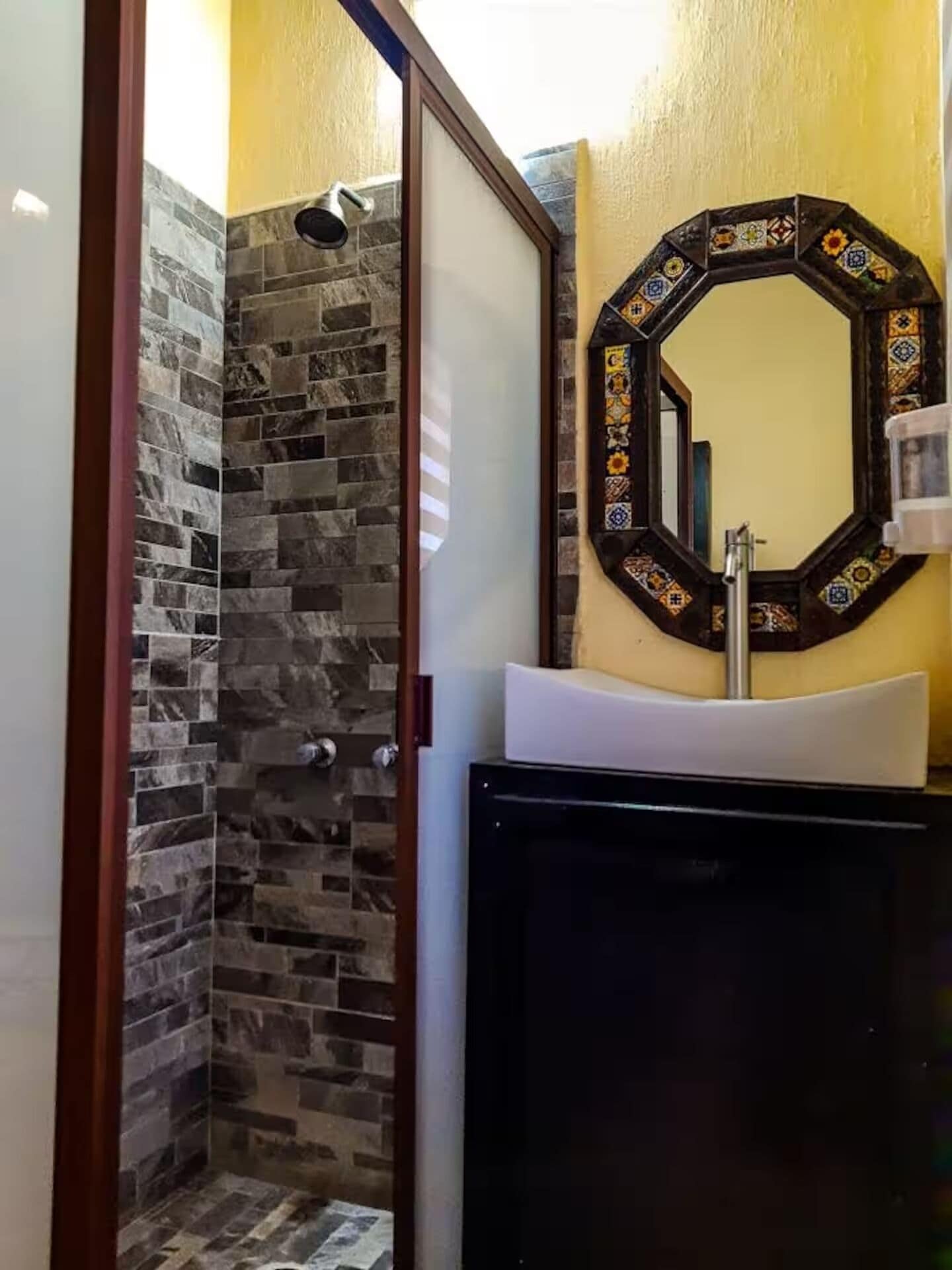 Un bany amb una dutxa de pedra, un lavabo amb un mirall decoratiu i un armari.