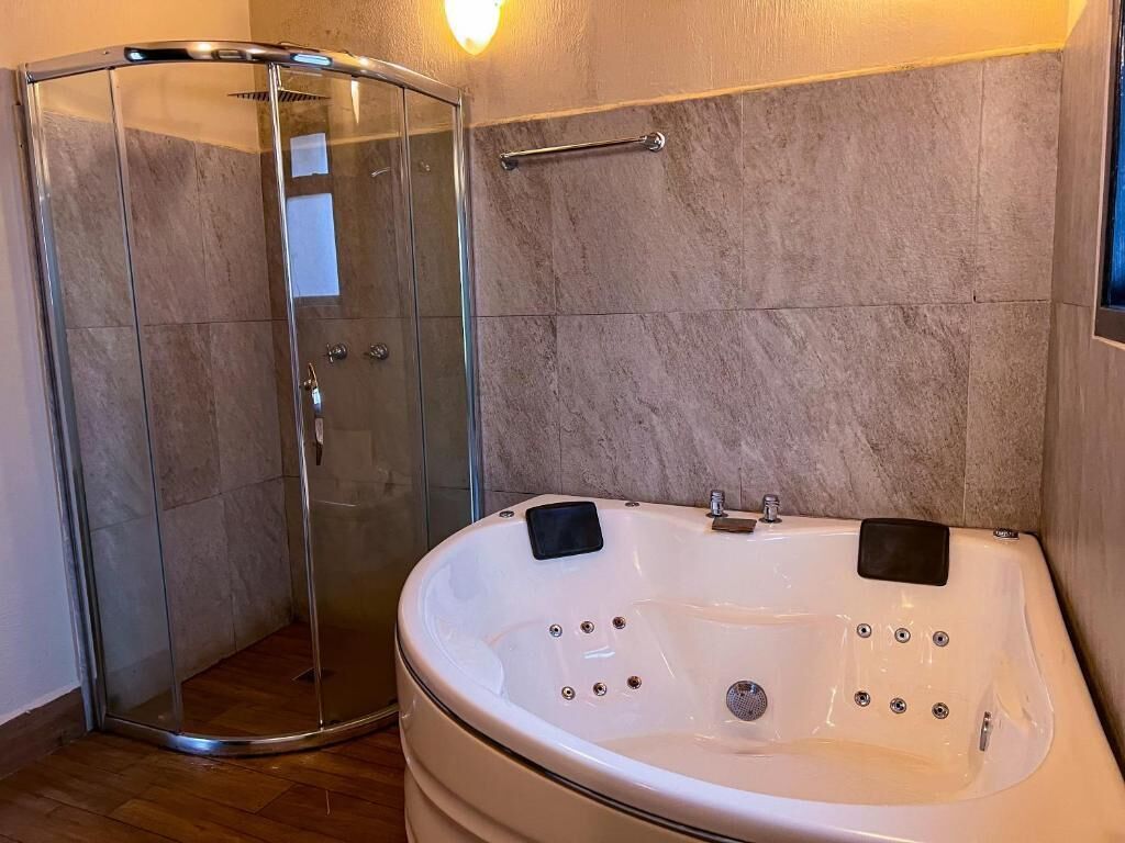 A bathroom with a glass-enclosed shower, a white bathtub with two black seats, and a towel rack on the wall.