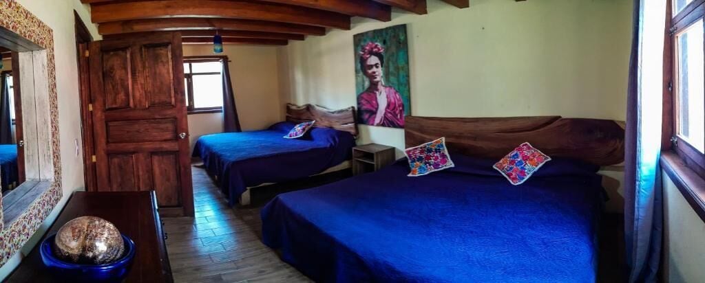 A room with two beds, wooden beams on the ceiling, a painting on the wall, and a wooden door.