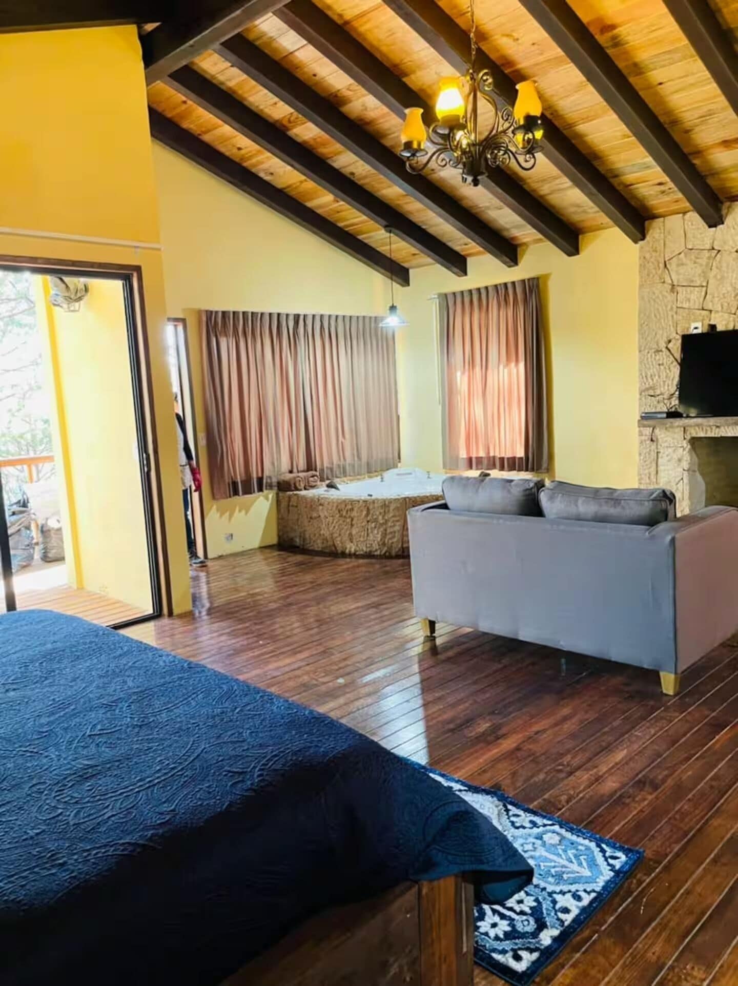 A spacious room with a large bed, a grey sofa, and a stone fireplace.