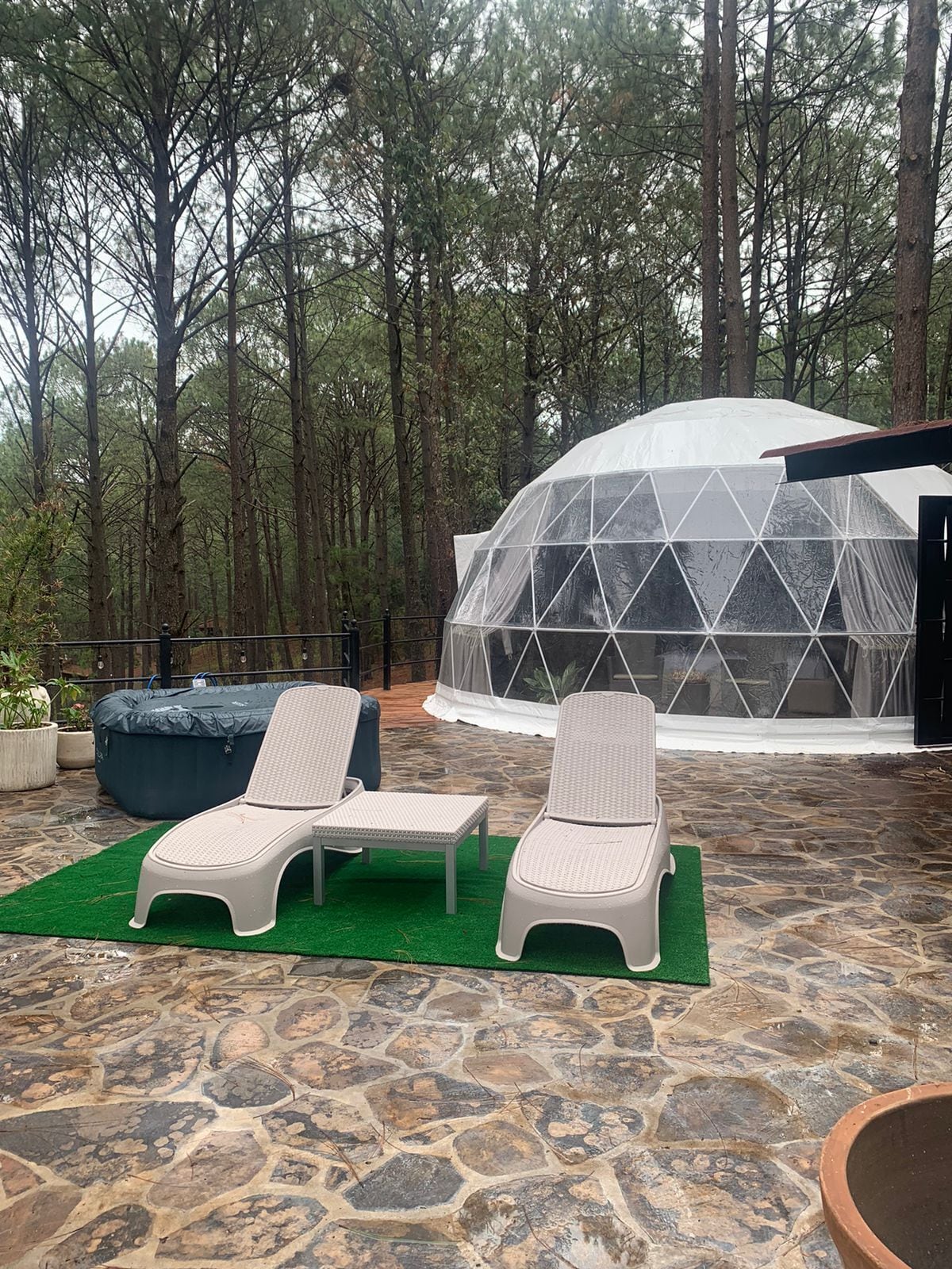Un pabellón con cúpula transparente y un patio de piedra con dos sillones de descanso.