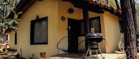Un petit bâtiment d’un seul étage, doté d’un toit en pente, d’un porche avec un barbecue et d’une chaise.