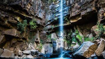 Uma cachoeira despencando de um penhasco rochoso em direção a um lago cercado por grandes pedras.