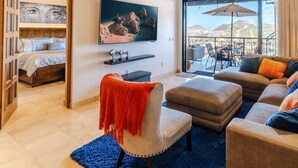 Un salon spacieux avec une grande télévision, un balcon doté d’un coin salon extérieur et une vue sur les montagnes.