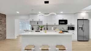 Une cuisine moderne avec des meubles blancs, un îlot central doté de tabourets, un réfrigérateur en acier inoxydable et un four à micro-ondes.