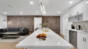 Une cuisine moderne dotée d’un îlot en marbre, d’un mur d’accent en briques et d’un coin repas comprenant un canapé et une table basse.