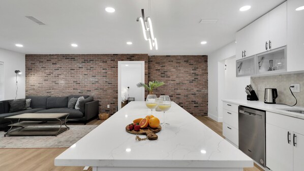 Una cocina moderna con una isla de mármol, una pared de acento de ladrillo y una zona de comedor con sofá y mesa de centro.