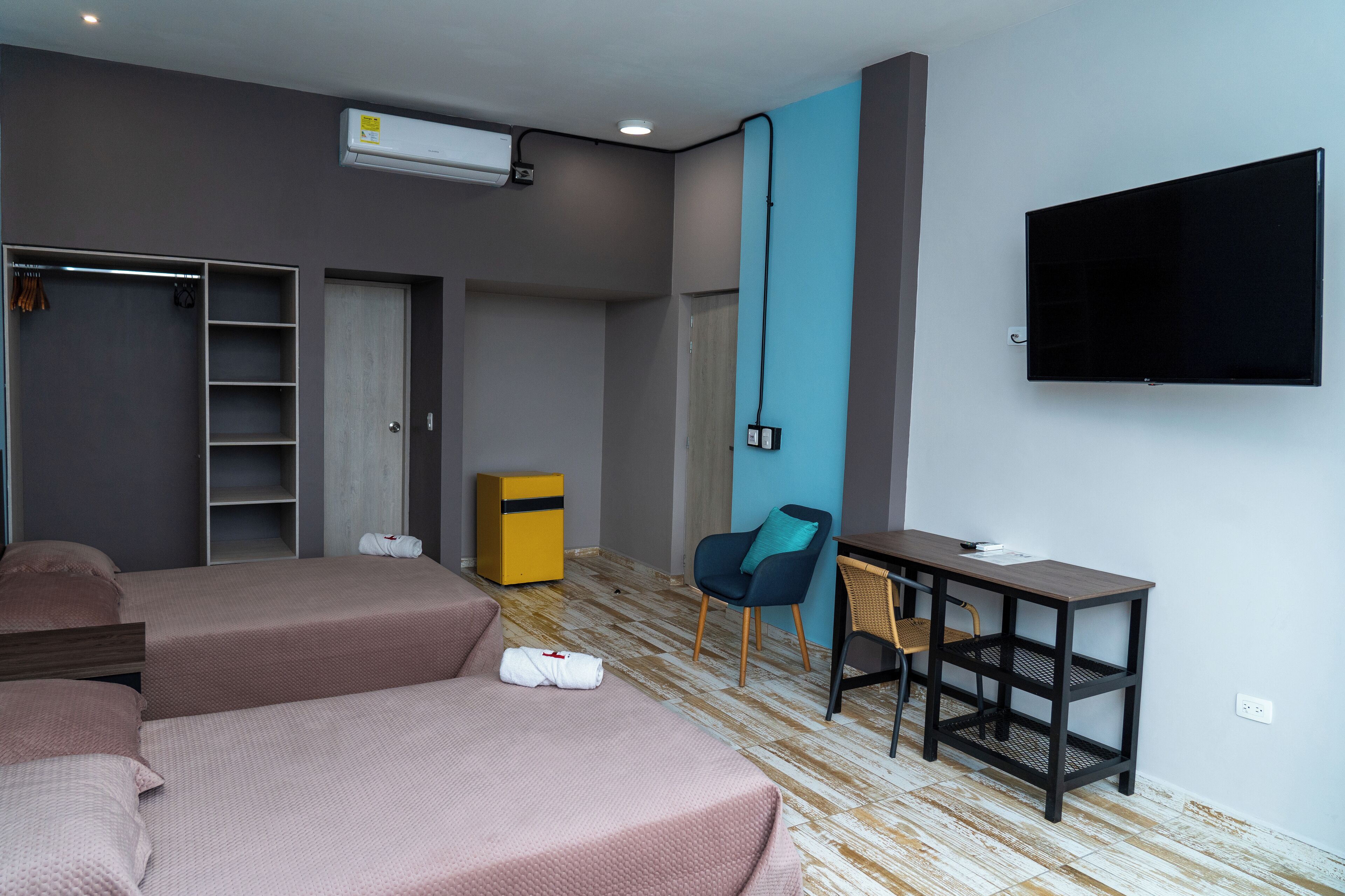 Habitación de hotel con dos camas, un escritorio, una silla, un armario y un televisor.