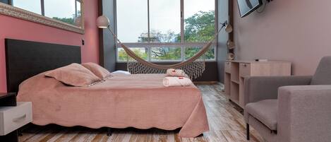 A bedroom with a bed, a hammock, a TV, and a chair.