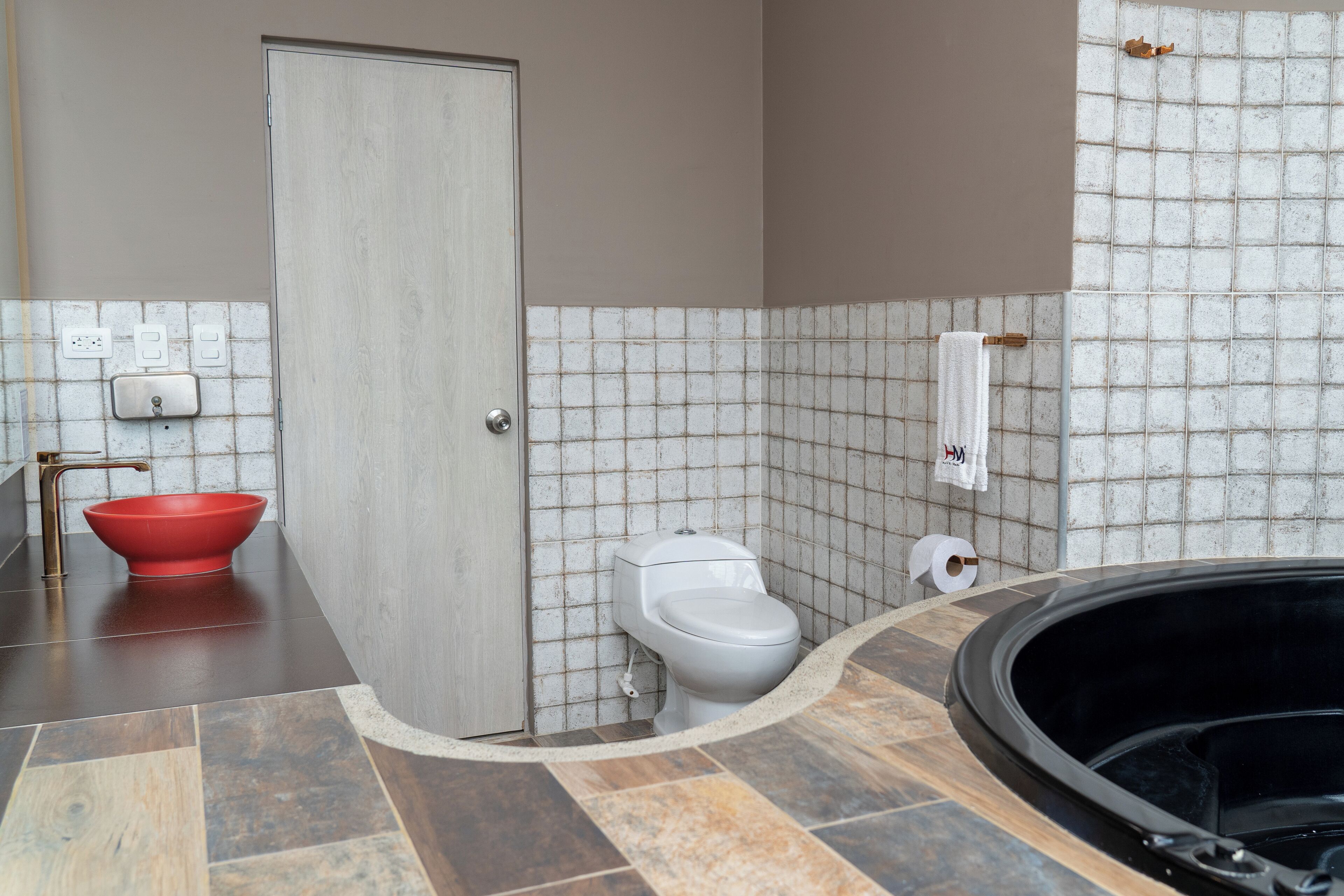 A bathroom with a red basin, white toilet, and a black bathtub.