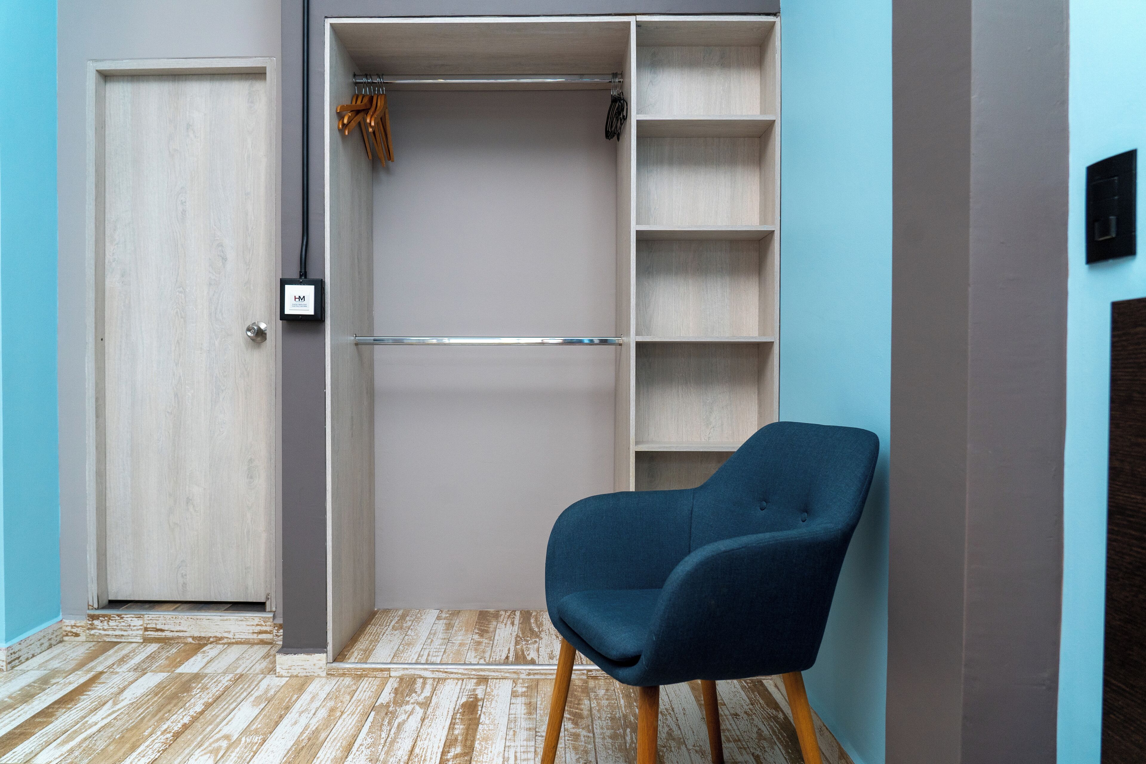 A room with a wardrobe, a blue chair, and a wooden floor.