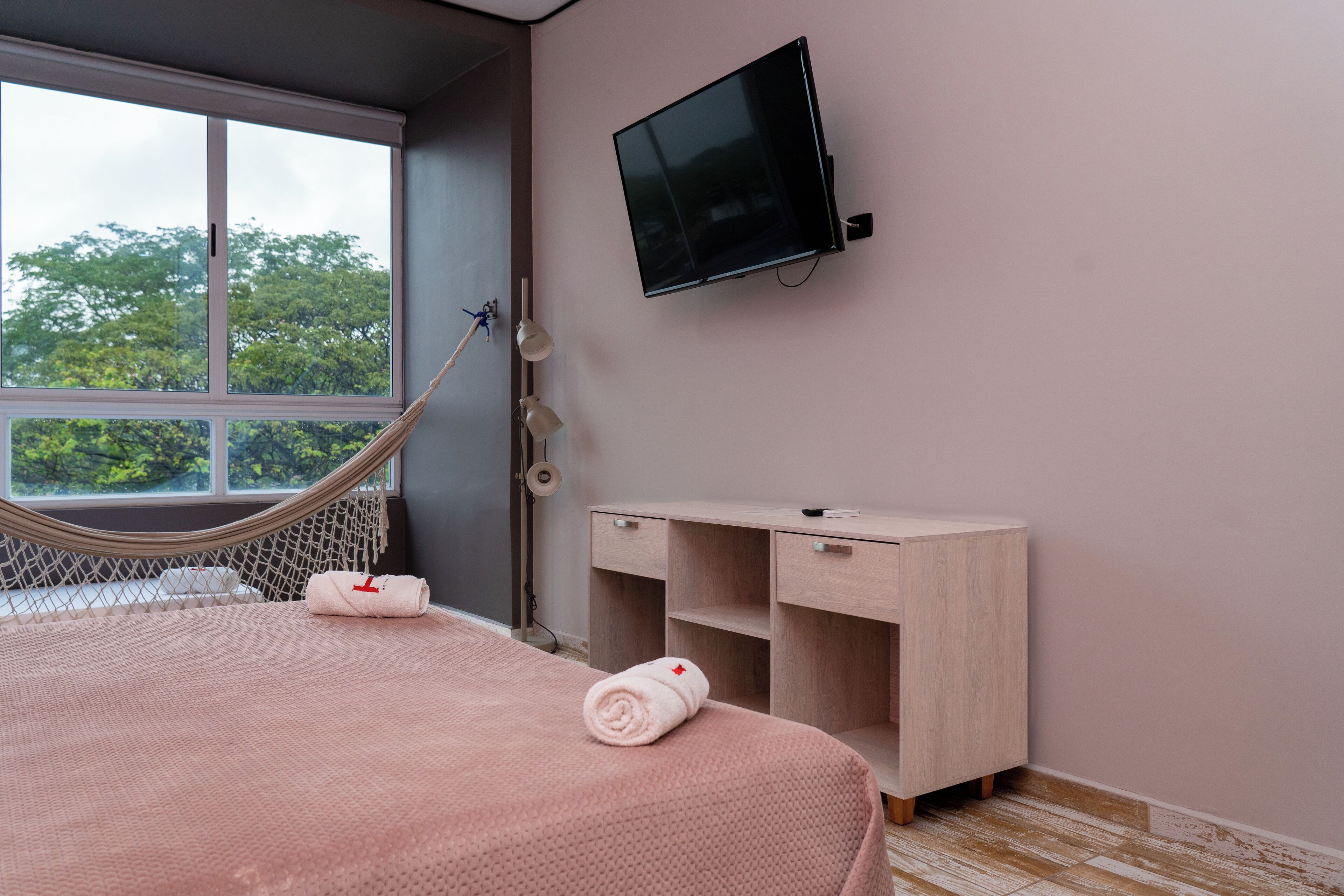 A bedroom with a bed, a desk, a TV, and a hammock.