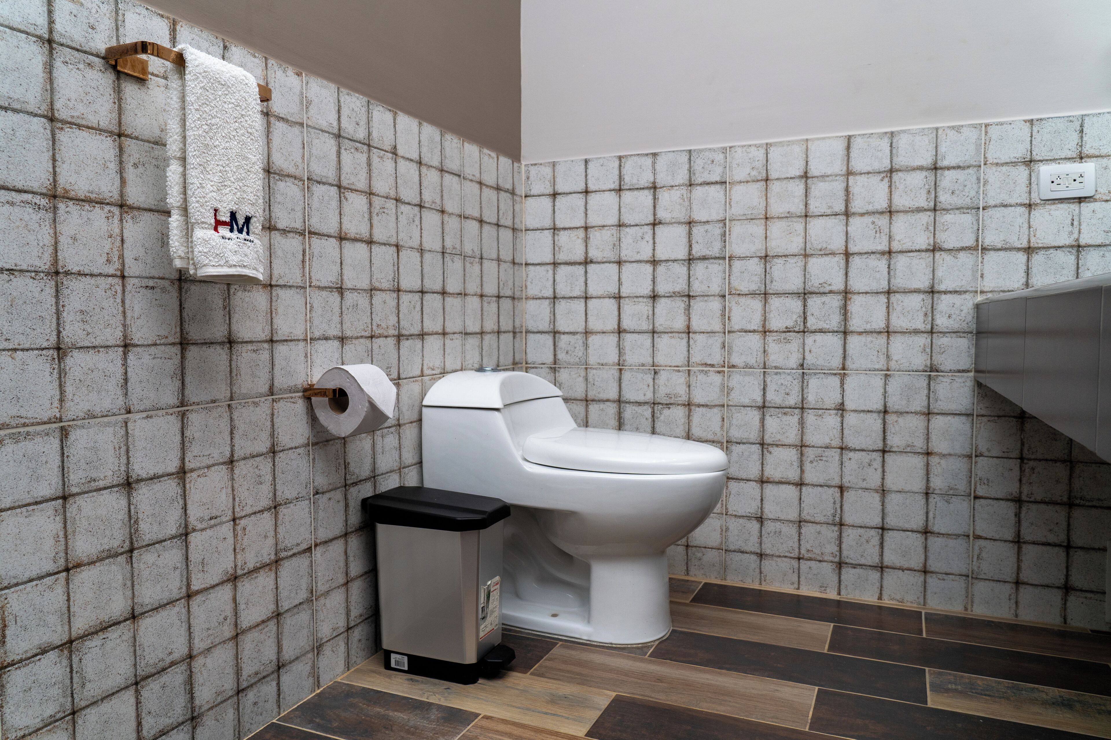 Un baño con inodoro, un bote de basura y una toalla colgada en un perchero.