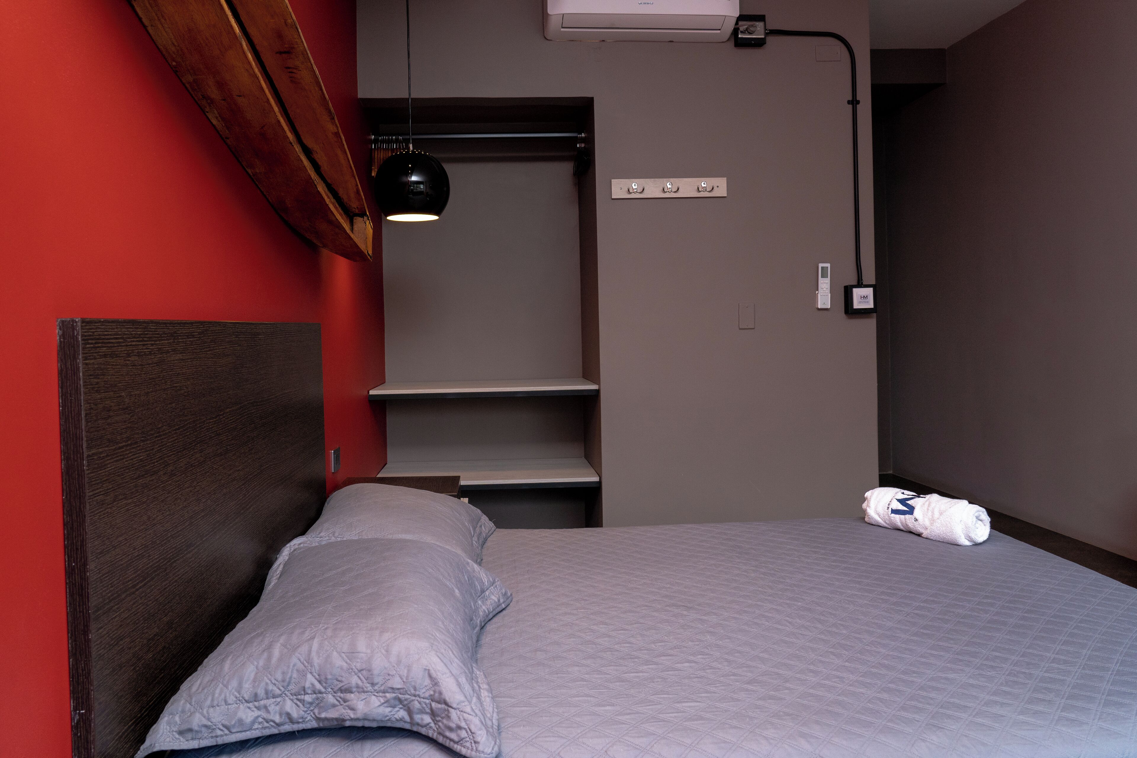A bedroom with a bed, a headboard, a bedside table, a lamp, and a wall-mounted shelf.