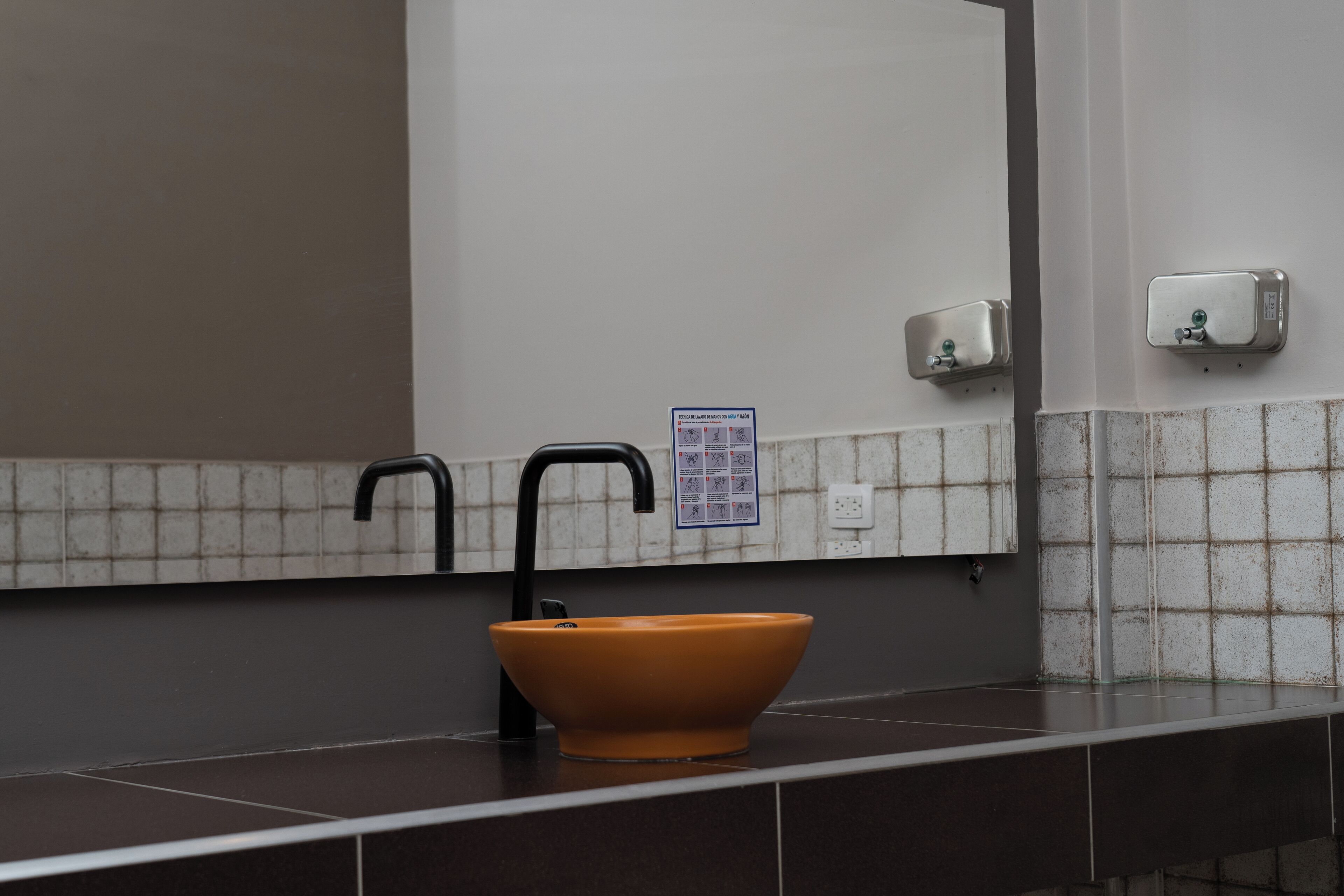 Un baño con un lavamanos marrón, grifos negros y un espejo encima.
