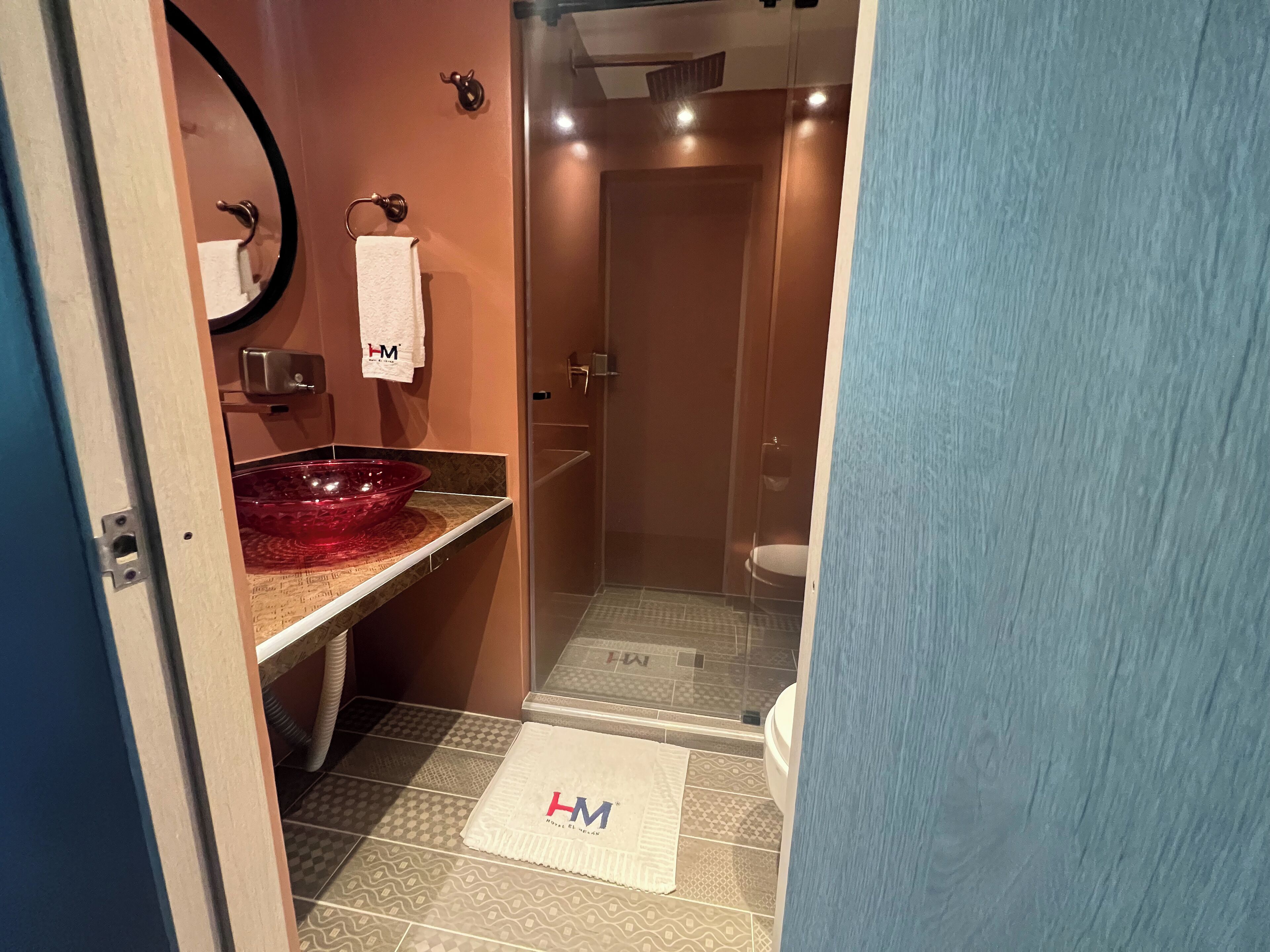 A bathroom with a glass-enclosed shower, a red glass sink, and a towel rack with a white towel.
