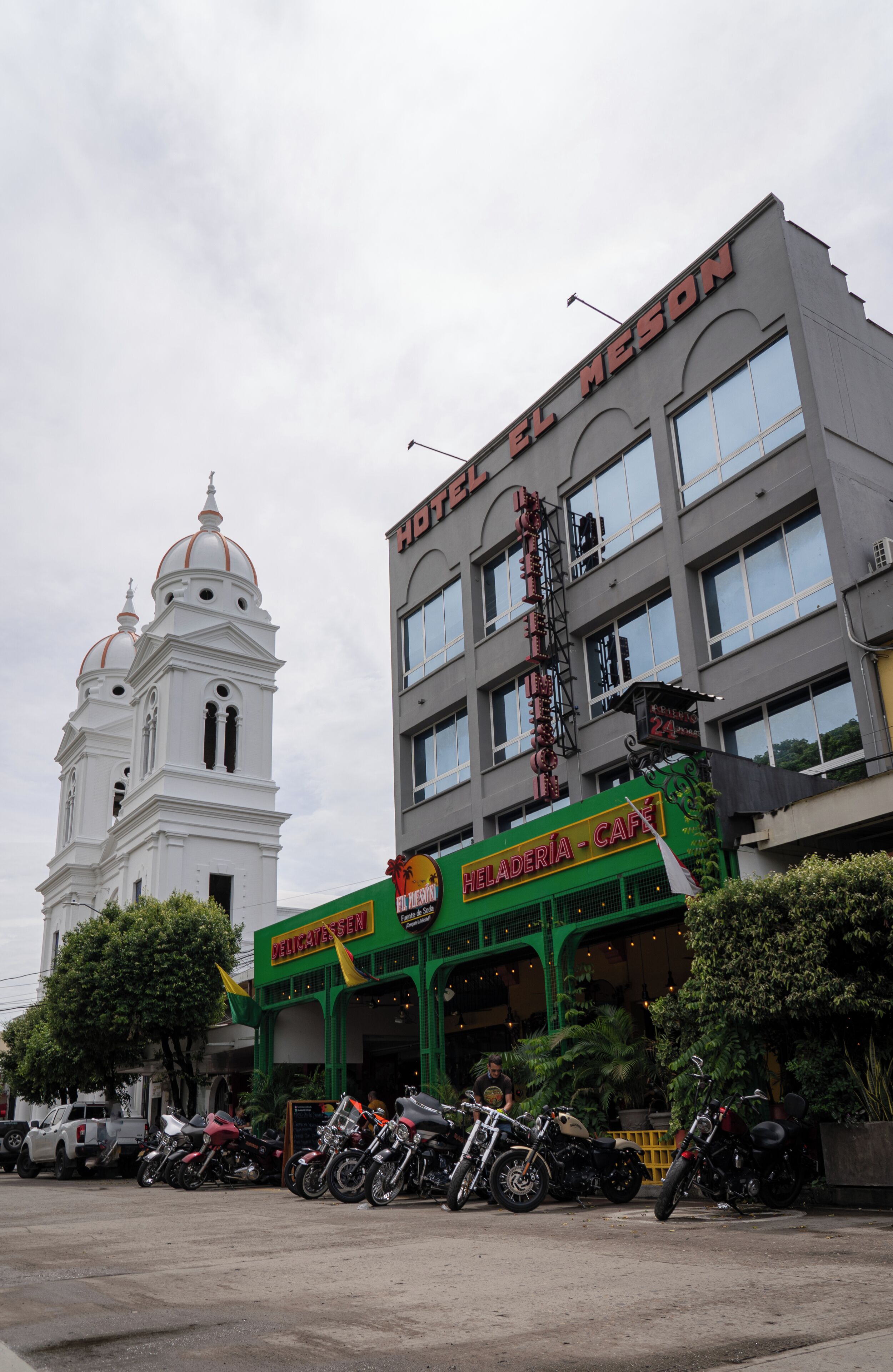 A hotel with a large sign reading "HOTEL EL MESON" and a cafe named "HELADERIA - CAFÉ" in front.