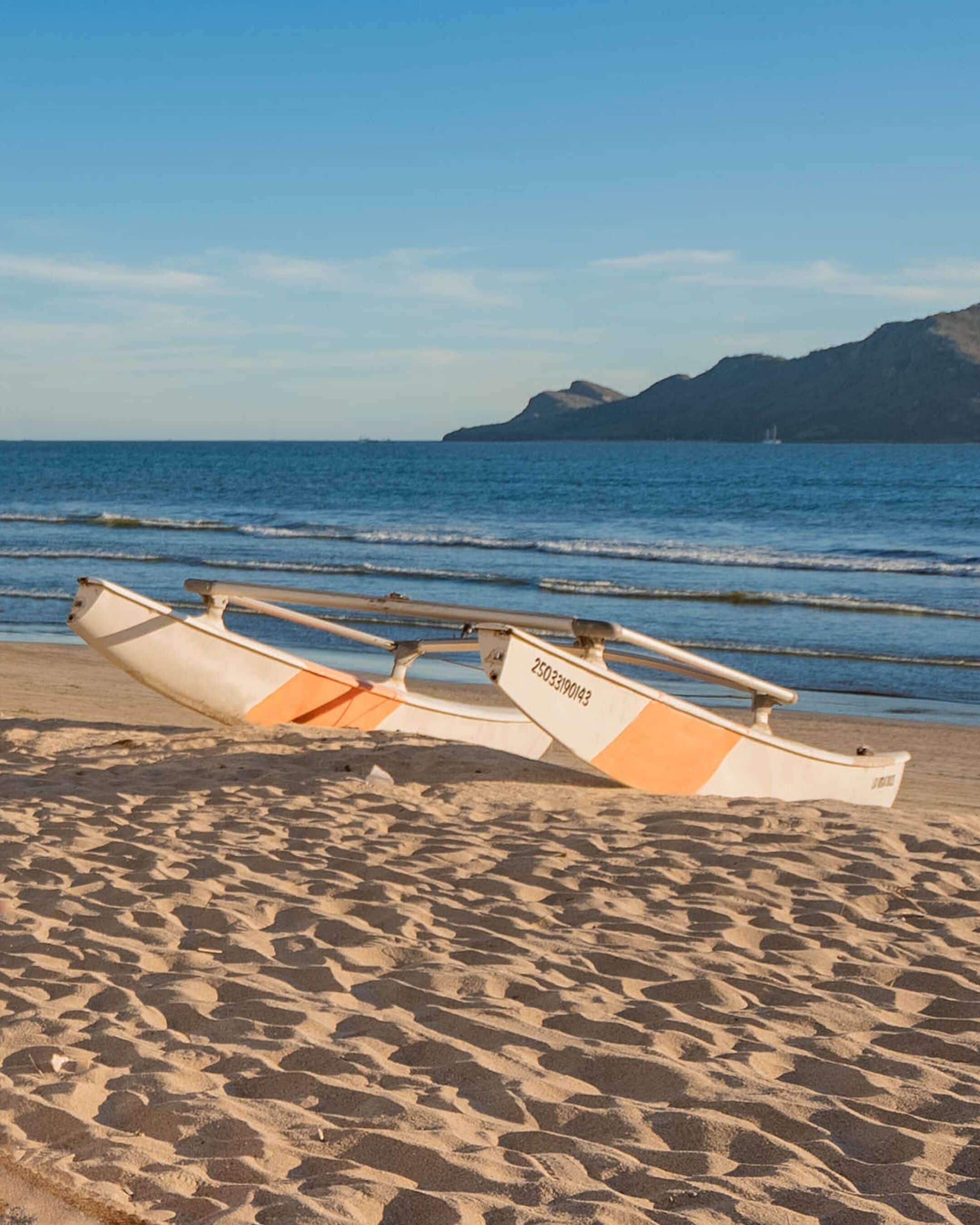 Two boats on a sandy beach with a calm sea and a mountain in the background.
