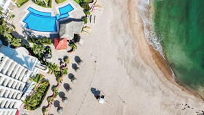 Eine Vogelperspektive eines Strandresorts mit Schwimmbad, Palmen und Sandstrand.