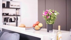 A modern kitchen with a white countertop, a bowl of fruit, a vase of flowers, and a bottle of wine. - Mad Hatter (Roma)