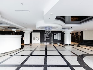 A spacious lobby with a marble floor, a reception desk, and a modern chandelier.