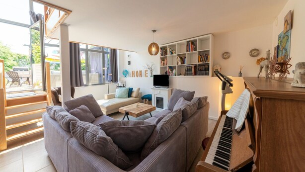 A modern living room with a sectional sofa, a piano, a bookshelf, and a large window. - Magnificent Holiday Home for 6 Adults in Xhoffraix (Malmedy)