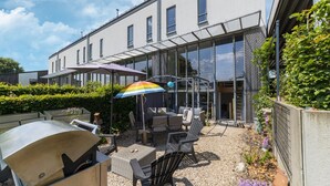 An outdoor patio with a grill, seating area, and a glass-enclosed space. - Magnificent Holiday Home for 6 Adults in Xhoffraix (Malmedy)