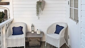 Une véranda avec deux fauteuils en osier, une petite table et un pot de fleurs suspendu.