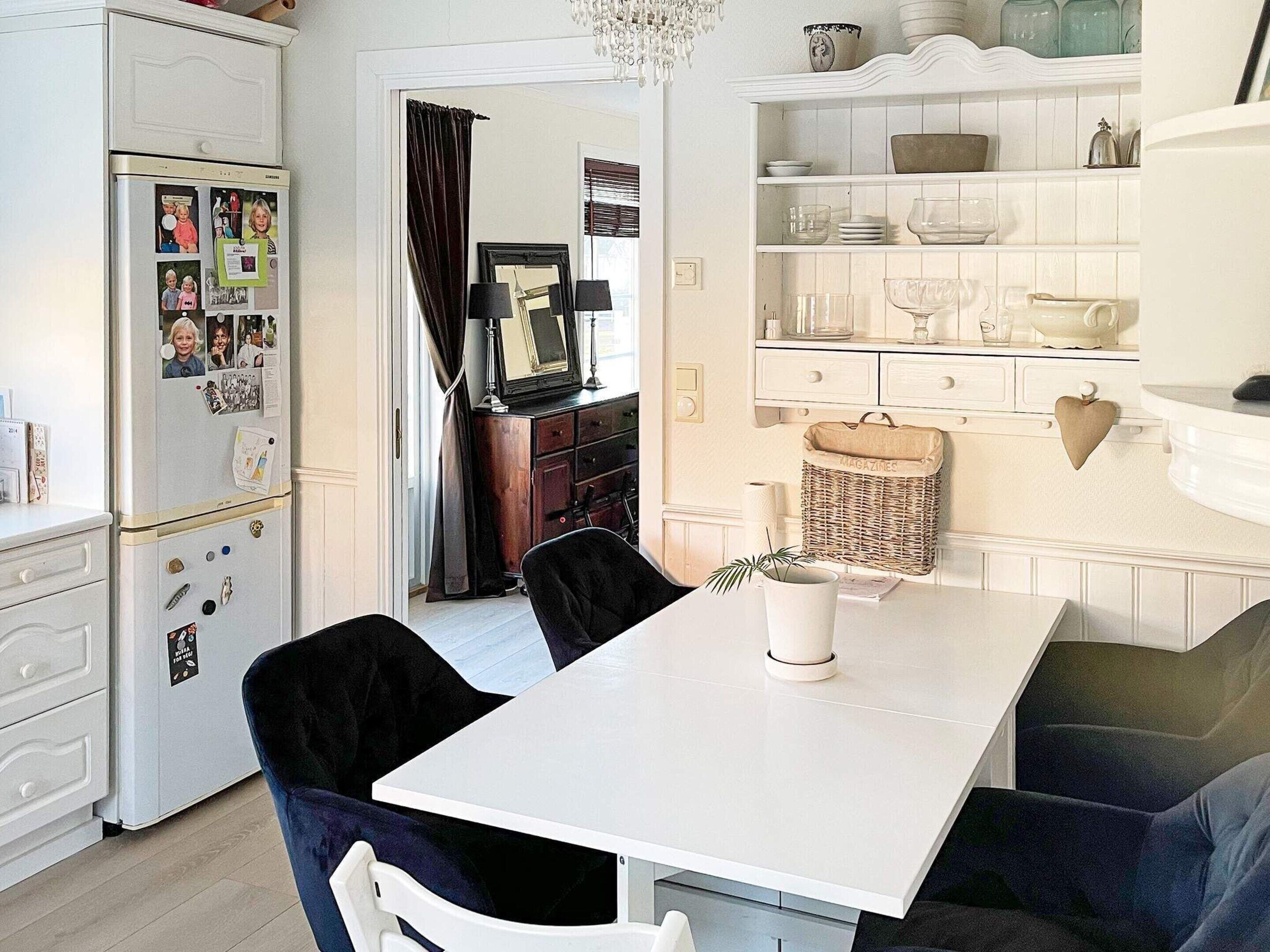 A modern kitchen with a white refrigerator, a dining table with chairs, and a wicker basket labeled 'MAGAZINES'.