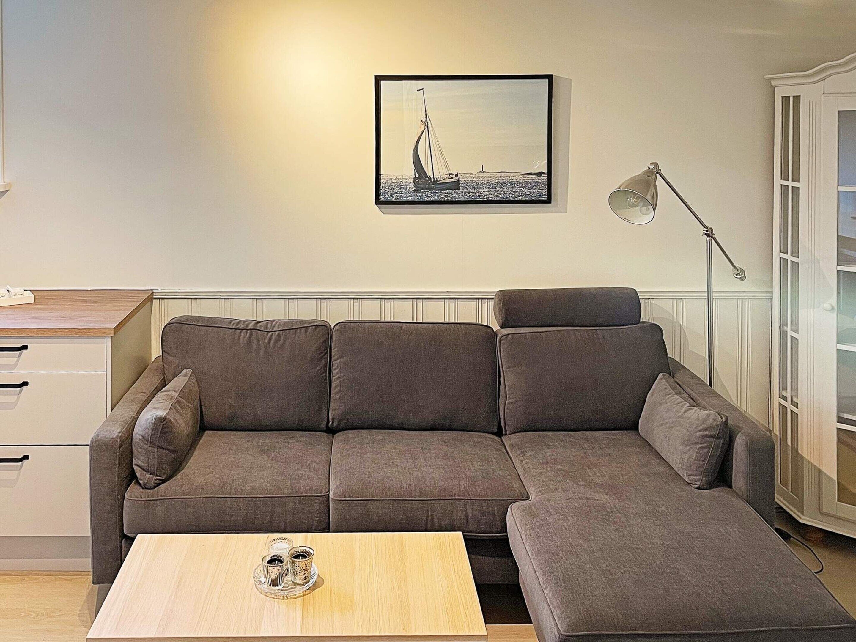 Una sala de estar con un sofá seccional marrón, una mesa de centro de madera, un cuadro enmarco con una imagen de un velero y una lámpara de pie.