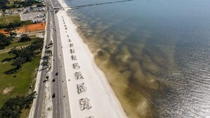 Vista aèria d'una carretera costanera amb una platja d'un costat i un moll que s'endinsa a l'aigua.