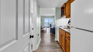 A modern kitchen with wooden cabinets, a white refrigerator, and a window overlooking a balcony. - Bluewater Resort 207 (Myrtle Beach)