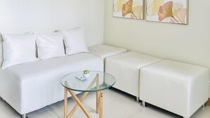 A modern, minimalist room with a white sofa, a glass coffee table, and two wall-mounted paintings. - Exclusive 1BR Residences at LaFayette Park Square (Iloilo City)