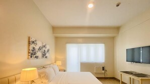 A hotel room with a bed, bedside lamp, artwork, air conditioning unit, and a TV. - Exclusive 1BR Residences at LaFayette Park Square (Iloilo City)