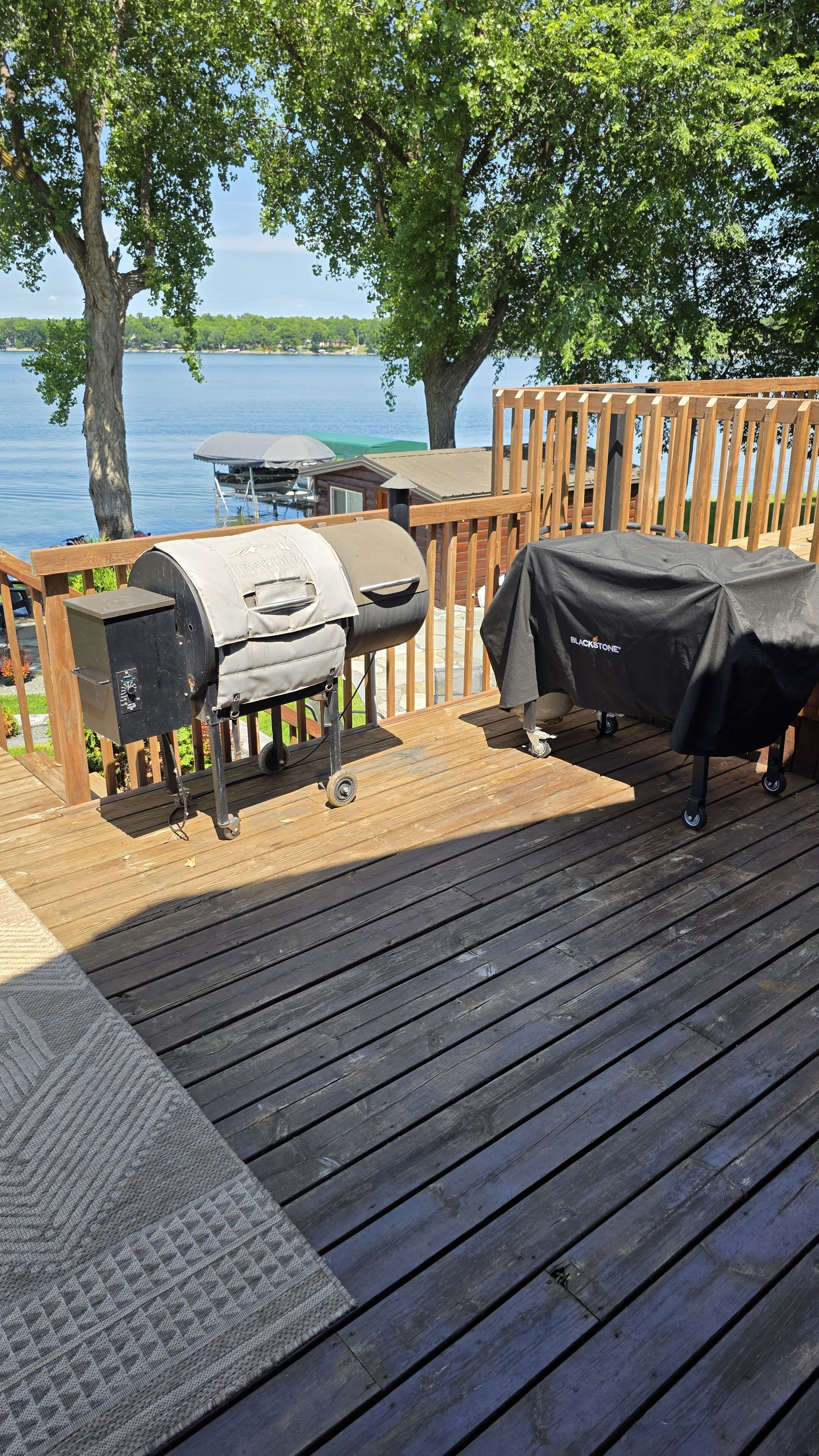 Eine Holzterrasse mit Grill und Grillutensilien mit Blick auf einen See.