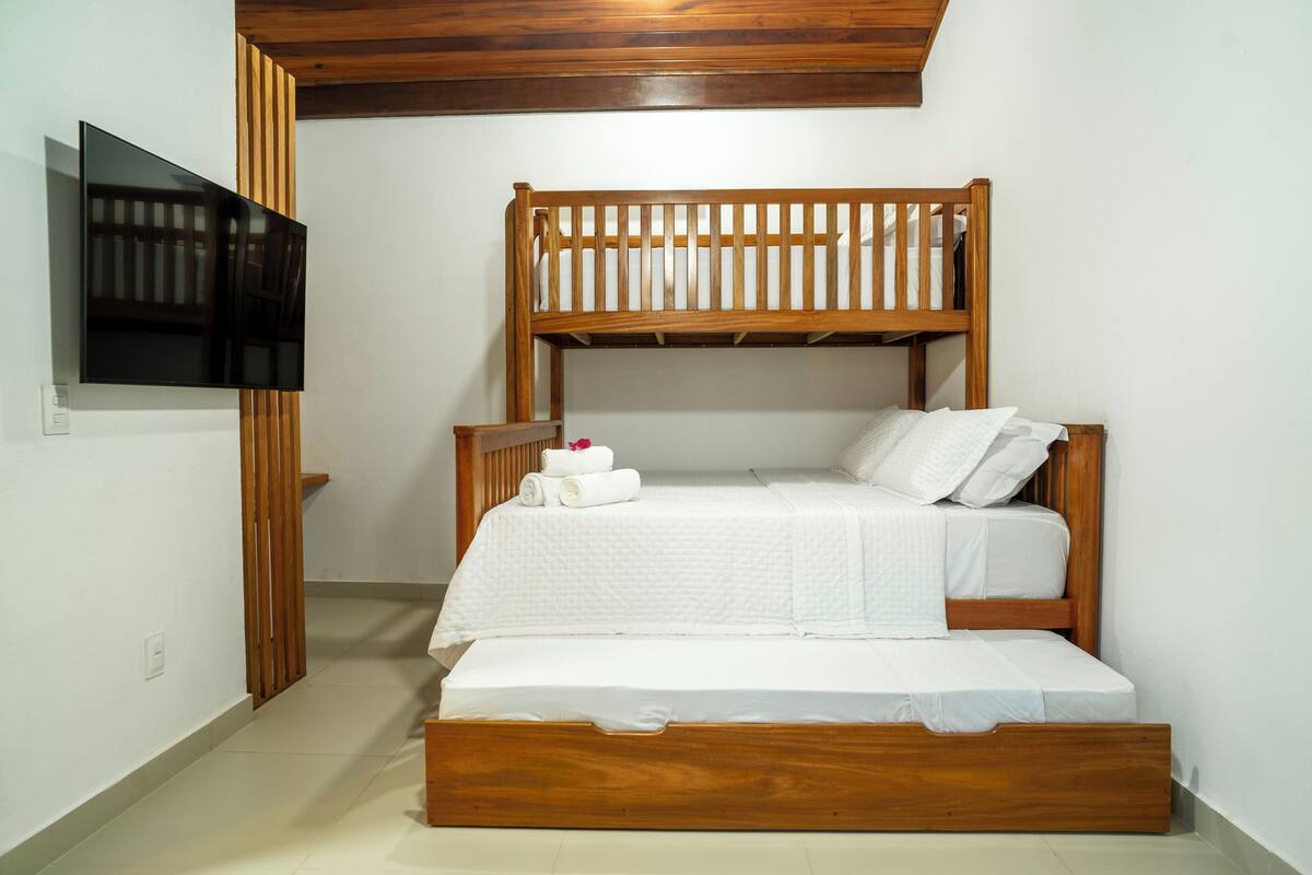 Un lit superposé avec un téléviseur fixé au mur, un lambris en bois et une couvre-lit blanche.