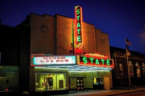 Ein Theater mit einer Neonreklame, die "STATE" und "DAS SECHSTE GEFÜHL" anzeigt, mit dem Preis 3 Dollar und einer Vorstellung um 21:30 Uhr.