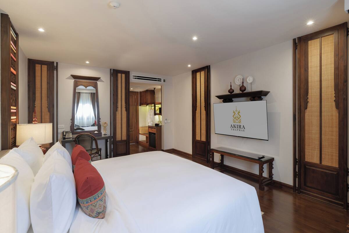 Quarto de hotel com uma cama grande, uma escrivaninha, uma cadeira, uma televisão e um guarda-roupa.