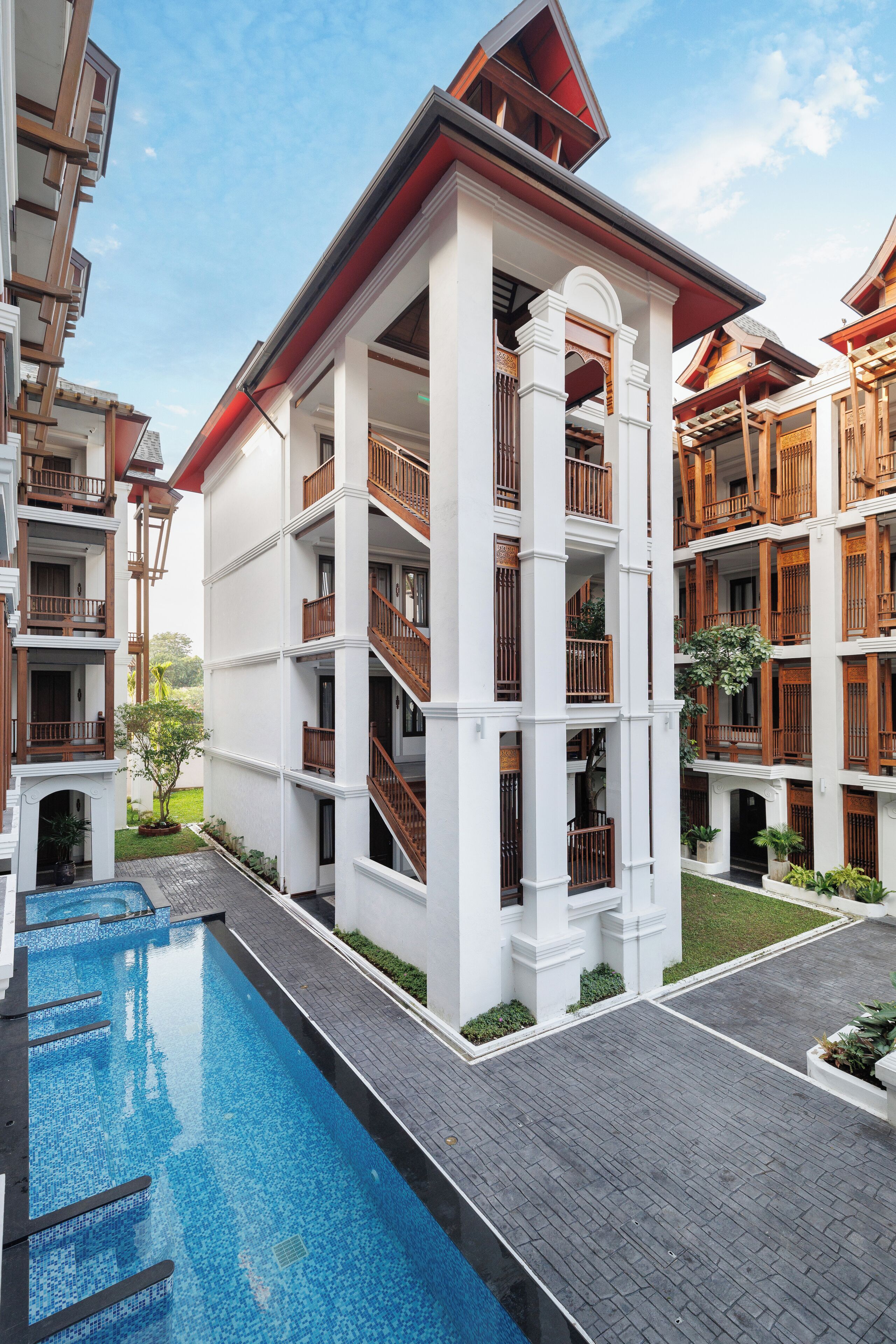 A multi-story hotel with a swimming pool, balconies, and a garden area.