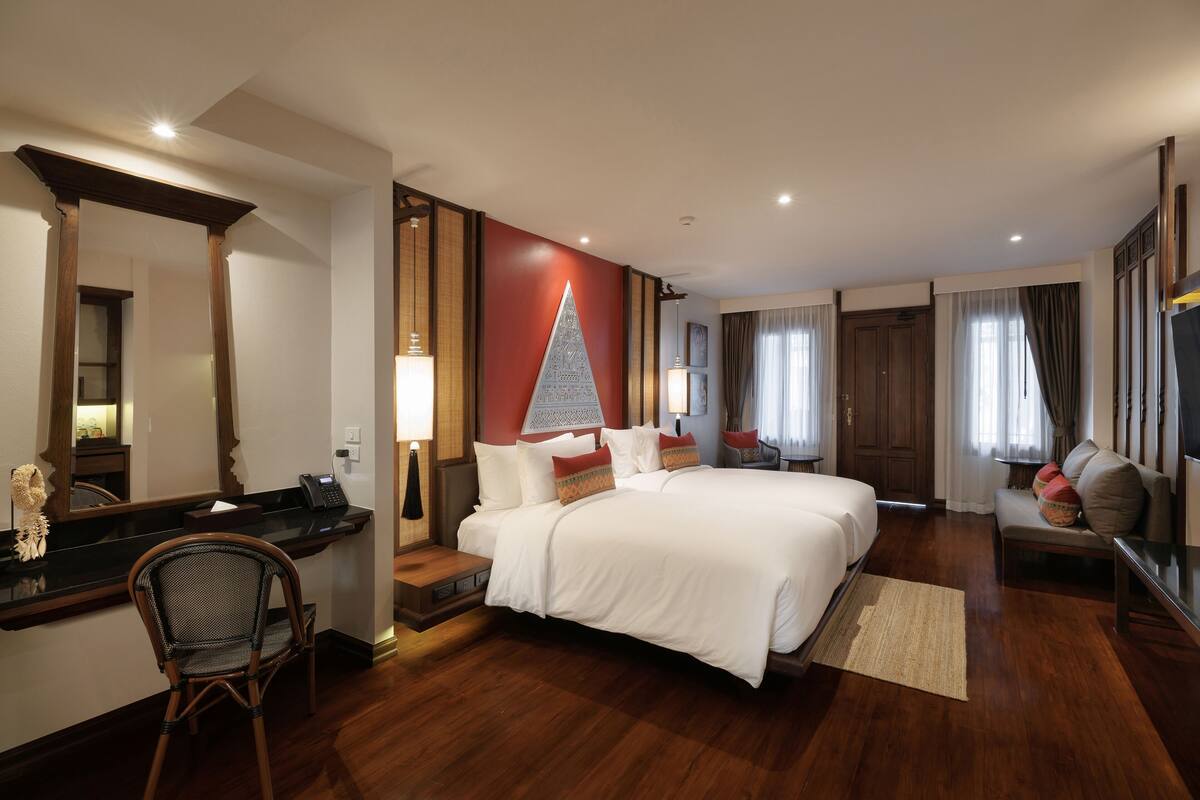 Quarto de hotel com uma cama grande, uma escrivaninha com cadeira, um espelho e uma parede decorada em vermelho.